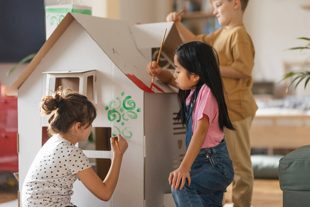 Happy children painting handmade carboard house together, having fun. - Fotoğraf, Görsel