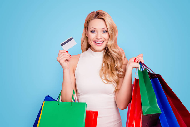 Portrait of girlish glad chick, excited positive girlfriend holding colorful packets in hands showing gesturing plastic credit card isolated on pink background. - Foto, Imagem