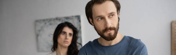 Dissatisfied bearded man looking away near blurred girlfriend at home, banner  - Foto, immagini