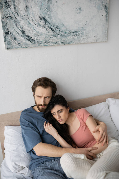 Elégedetlen férfi pizsamában ölelkezik aszexuális barátnő az ágyban otthon  - Fotó, kép