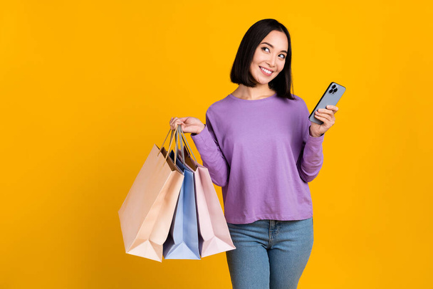 Photo of excited dreamy lady dressed purple shirt holding gadget rising bargains looking empty space isolated yellow color background. - Φωτογραφία, εικόνα