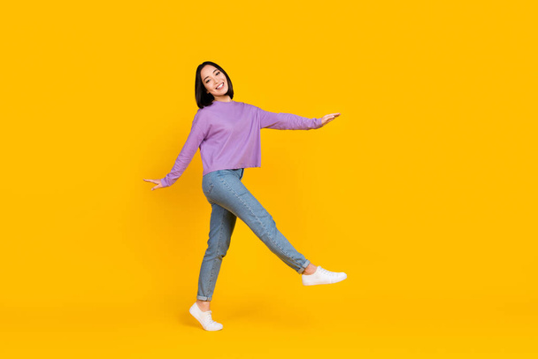 Full length photo of funky carefree lady dressed purple shirt walking empty space isolated yellow color background. - Foto, Imagen