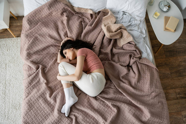 Draufsicht einer depressiven Frau im Pyjama, die zu Hause auf dem Bett liegt  - Foto, Bild