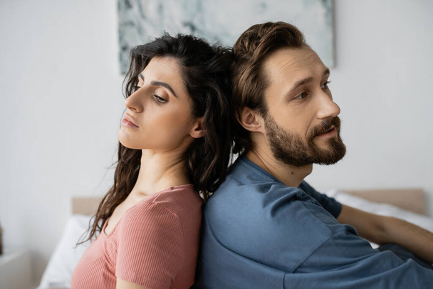 Triste pareja sentada espalda con espalda en el dormitorio borroso en casa  - Foto, imagen