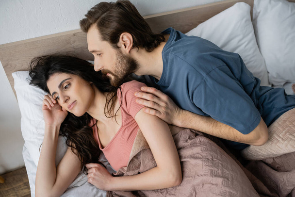 Vysoký úhel pohledu na vousatý muž při pohledu na lhostejné přítelkyně v posteli v dopoledních hodinách  - Fotografie, Obrázek