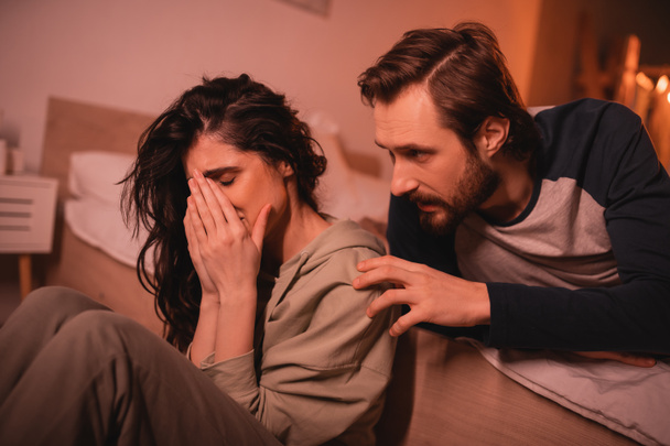 Mujer llorando recibiendo atención de novio barbudo en el dormitorio por la noche  - Foto, Imagen