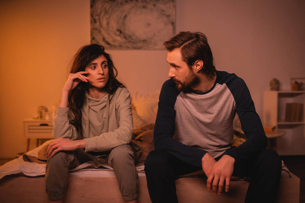 Dissatisfied woman talking to bearded boyfriend on bed in evening  - Photo, Image