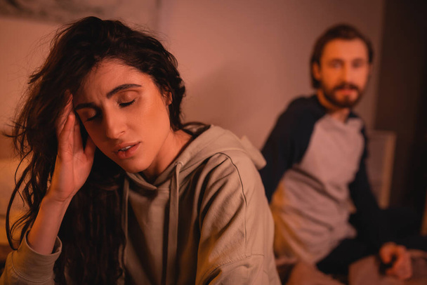 Dissatisfied woman touching head near blurred boyfriend at home  - Fotó, kép