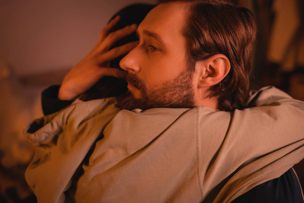 Caring man hugging girlfriend at home with red lighting in evening  - Photo, Image