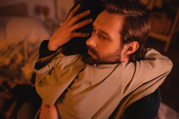 Bearded man hugging girlfriend at home with red lighting   - Photo, Image