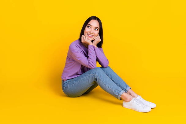 Photo of good mood dreamy woman wear violet shirt siting floor looking empty space isolated yellow color background. - Zdjęcie, obraz