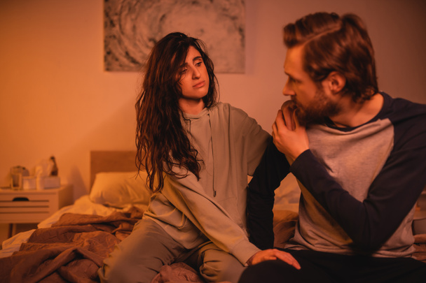 Dissatisfied woman looking at blurred boyfriend sitting on bed at night  - Fotografie, Obrázek