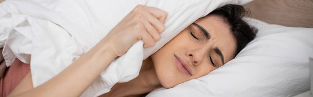 Δυσαρεστημένη γυναίκα που βάζει μαξιλάρι στο κεφάλι στο κρεβάτι το πρωί, πανό  - Φωτογραφία, εικόνα