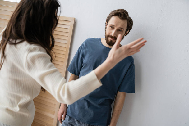 Frustrated man in pajama standing near blurred girlfriend quarrelling at home  - Foto, Imagem