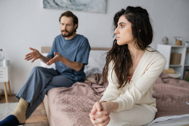 Offended woman sitting near blurred boyfriend talking during relationship difficulties at home  - Photo, Image
