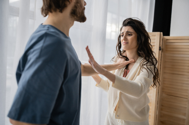 Scared woman showing stop gesture near abusive boyfriend at home  - Fotografie, Obrázek
