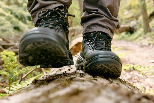 Traveler man has hiking in mountain forest. Close up of human foots in mountain shoe walking on tree log. Exercise and fitness in nature for wellness and healthy lifestyle. - Фото, зображення
