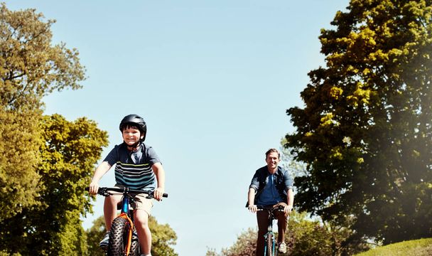 Ścigamy się do końca, tato. młody chłopiec i jego ojciec jadący razem na rowerach - Zdjęcie, obraz