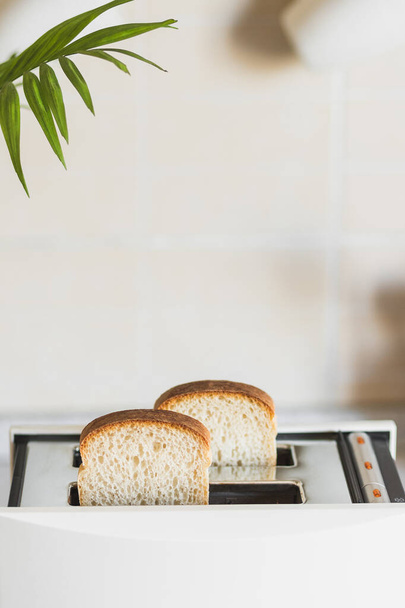 Weißer Toaster mit Weißbrot in heller Küche, hoher Schlüssel, vertikaler Kopierraum. - Foto, Bild