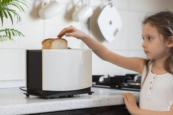 Tyttö kokkaa keittiössä. Valkoinen leivänpaahdin viipaloitu leipä seisoo työtasolla keittiön pöydän. - Valokuva, kuva