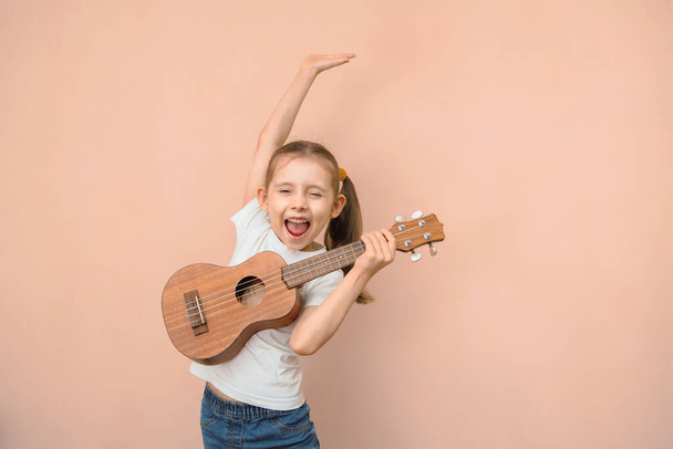 Expressive emotional Caucasian girl of primary school age learns music by playing the childrens guitar. - Photo, Image