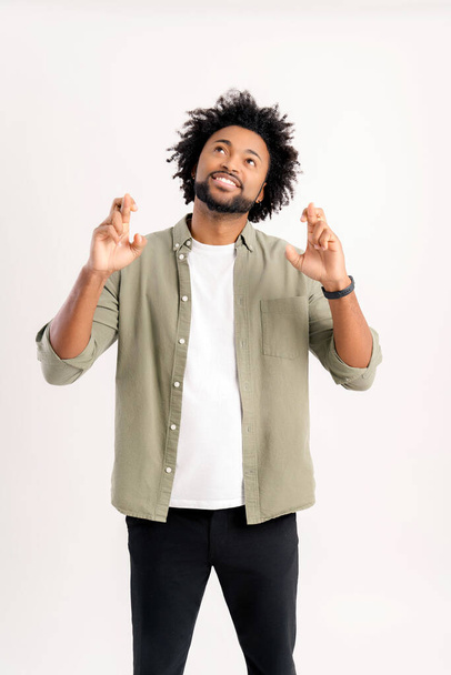 Wish you good luck. Handsome 30s curly guy in casual shirt holding fingers crossed isolated on white, charismatic african-american man hoping for miracle, strong wishing something, praying - Foto, immagini