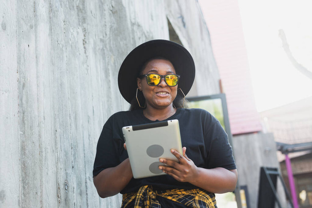 Portret pięknej, kręconej Afroamerykanki stojącej w tle miasta i trzymającej cyfrowy tablet. urocza młoda kobieta z koncepcją tabletu - Zdjęcie, obraz