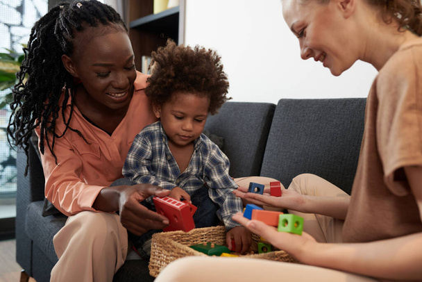 Весёлые матери показывают коробку с новыми красочными деревянными игрушками малышу - Фото, изображение