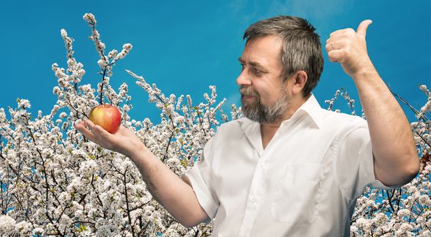 man van middelbare leeftijd in witte shirt met rode appel - Foto, afbeelding