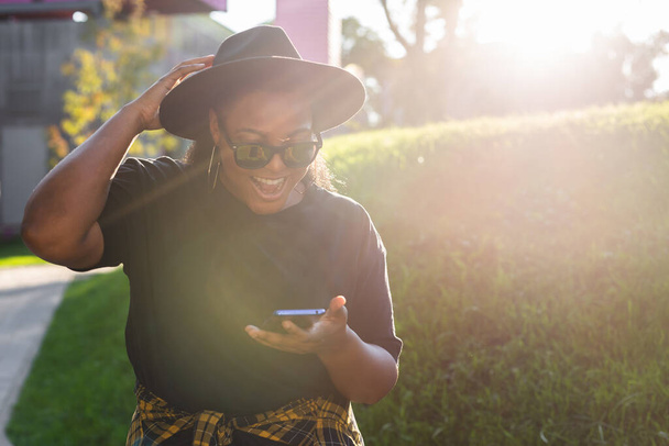 Κοντινό πορτραίτο μιας χαρούμενης αφροαμερικάνας νεαρής γυναίκας που μιλάει με κινητό τηλέφωνο στην πόλη - Φωτογραφία, εικόνα