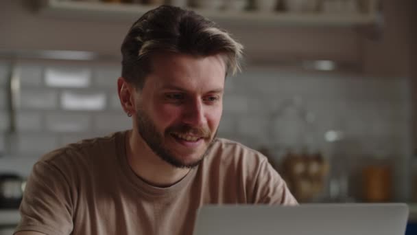 Zicht op een jongeman die aan een computer werkt. Lachende mannelijke freelancer werkt op afstand op laptop terwijl hij thuis zit. Hoge kwaliteit 4k beeldmateriaal - Video