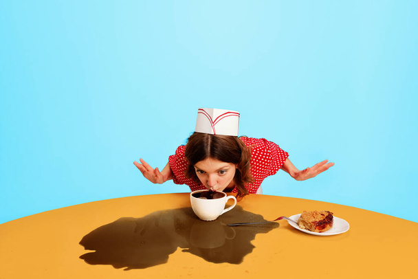 One young woman, strange waitress in 70s, 80s retro fashion style uniform sitting at table with coffee on vivid blue background. Trash pop art, retro palette. Concept of vintage, fashion, emotions, ad - Fotografie, Obrázek