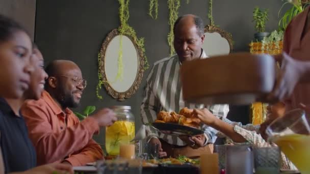 homme afro-américain joyeux donnant poulet frit aux invités à la maison familiale dîner - Séquence, vidéo