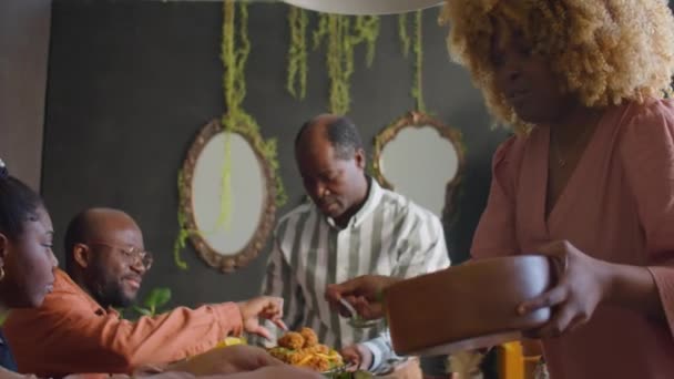Africká Američanka dávat salát na talíře pro členy rodiny při večeři doma - Záběry, video