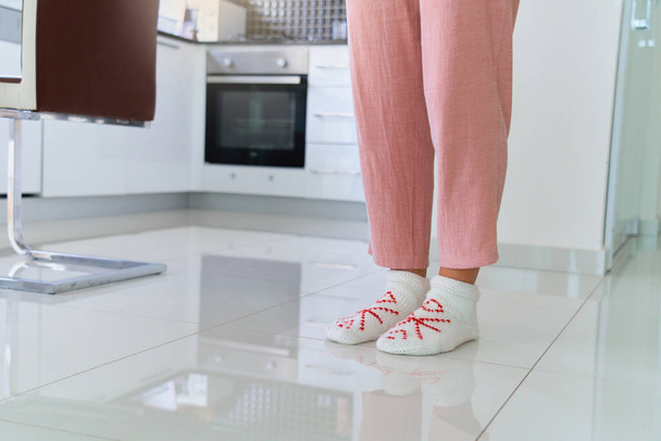 Female legs wearing cozy comfortable soft knitted socks on heated warm floor at home kitchen  - Фото, зображення