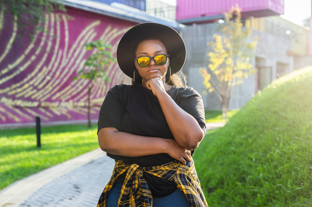 Αφροαμερικανή σε μια αστική περιοχή της πόλης. γενιά z ή χιλιετή hipster κορίτσι που θέτουν υπαίθρια backlight με το πορτρέτο του ήλιου - Φωτογραφία, εικόνα