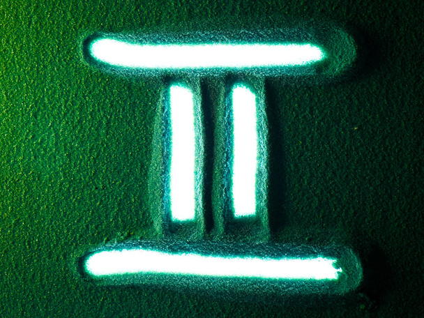 Handzeichnung des Zwillinge-Horoskop-Zeichensymbols im Grünen Sand. Männliche Hand schreibt das Widder-Horoskop-Zeichen auf den grünen Sand mit weißer Hintergrundbeleuchtung. 4k Auflösung von oben - Foto, Bild