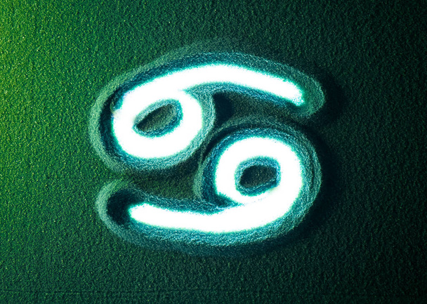 Handtekening van het symbool van de kankerhoroscoop in het groene zand. Mannelijke hand schrijft de Cancer horoscoop teken symbool op het groene zand met witte achtergrondverlichting. Top weergave 4k resolutie - Foto, afbeelding