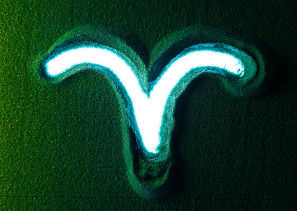 Yeşil Kum 'da Koç burcunun sembolünü elle çizmek. Erkek el, yeşil kuma beyaz arkaplan ışığıyla Koç burcunun burç sembolünü yazar. Üst görünüm 4k çözünürlüğü - Fotoğraf, Görsel