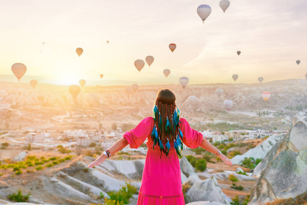 Alone spiritual free boho woman traveler makes wish in scenic valley in Anatolia, Kapadokya. Enjoying of flying hot air balloons at beautiful destination in Nevsehir, Goreme - Zdjęcie, obraz