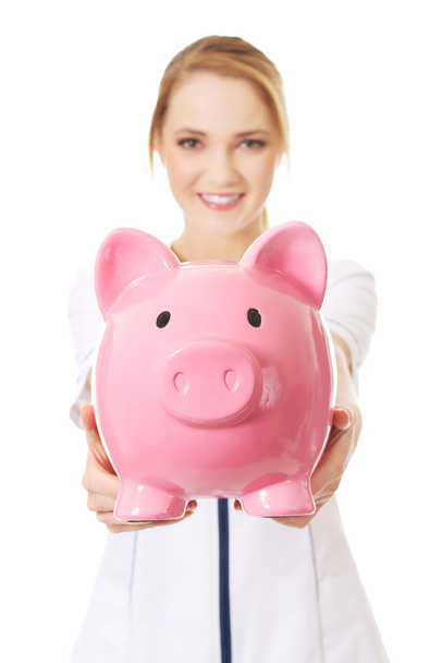 Young female doctor holding a piggybank. - Foto, imagen