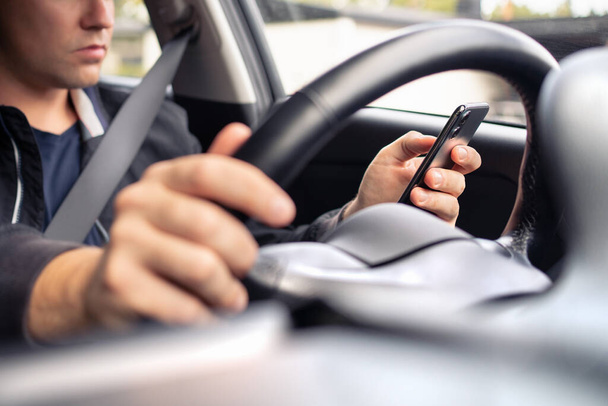 Texting and driving a car. Using mobile phone in traffic. Distracted driver, accident or crash. Irresponsible man typing sms text message with cellphone in city road or highway. Steering wheel. - 写真・画像