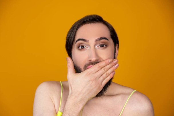Shocked astonished bearded transsexual person being amazed and excited covering mouth with hand posing isolated over orange background - Foto, imagen