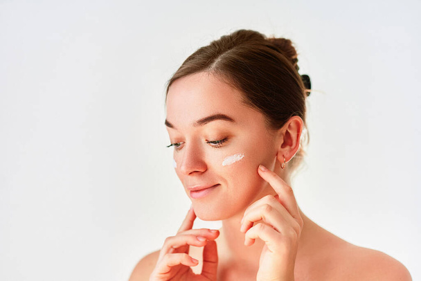 Young woman applying facial cream for beautiful healthy skin on white background - Foto, Imagem