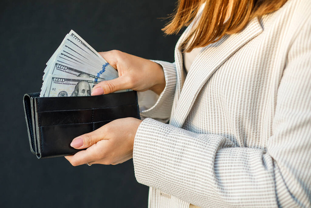 Młoda bizneswoman ukrywa dolary amerykańskie w czarnym portfelu, z bliska kobiece dłonie. - Zdjęcie, obraz