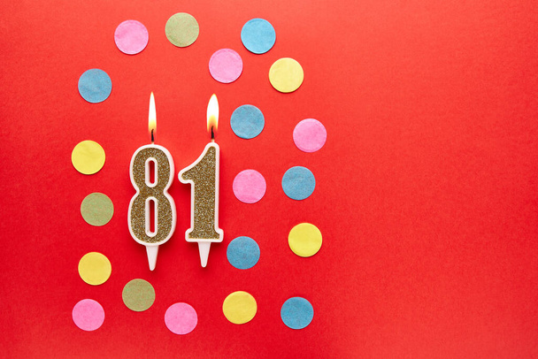 Number 81 on a red background with colored confetti. Happy birthday candles. The concept of celebrating a birthday, anniversary, important date, holiday. Copy space. banner - Foto, Imagem