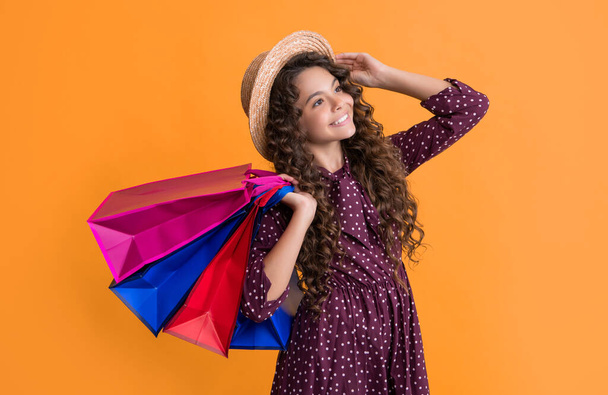 cheerful child with curly hair hold shopping bags on yellow background. - Foto, imagen