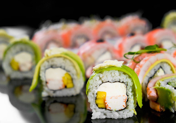Sushi heeft een zwarte achtergrond. Verse verscheidenheid aan broodjes in een Japans restaurant. Oosterse keuken. - Foto, afbeelding