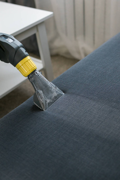 Pracovník úklidové společnosti odstraňuje nečistoty z nábytku v bytě s profesionálním vybavením. Muž rameno čištění pohovka s prací vysavač - Fotografie, Obrázek