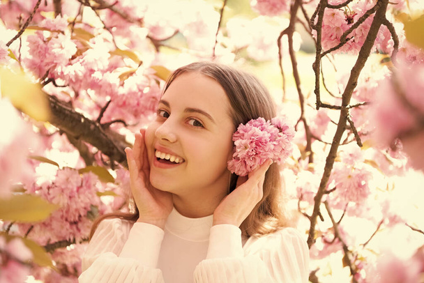 Portrait of happy girl child smiling at flowering cherry tree in spring. - Фото, изображение